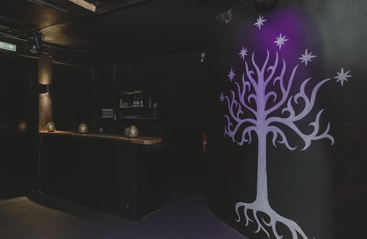 Bar neben einem violett beleuchteten Baummotiv an der Wand