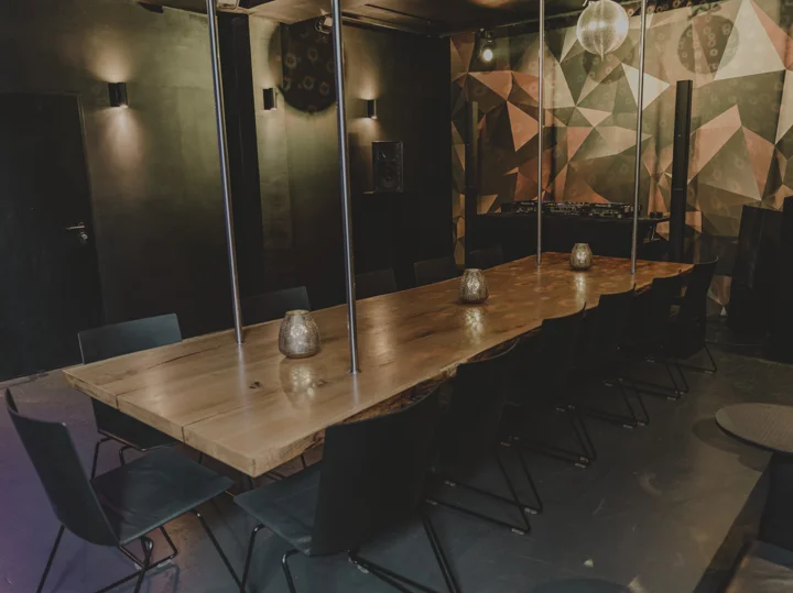Langer Holztisch mit schwarzen Stühlen und Kerzen im warm beleuchteten Raum